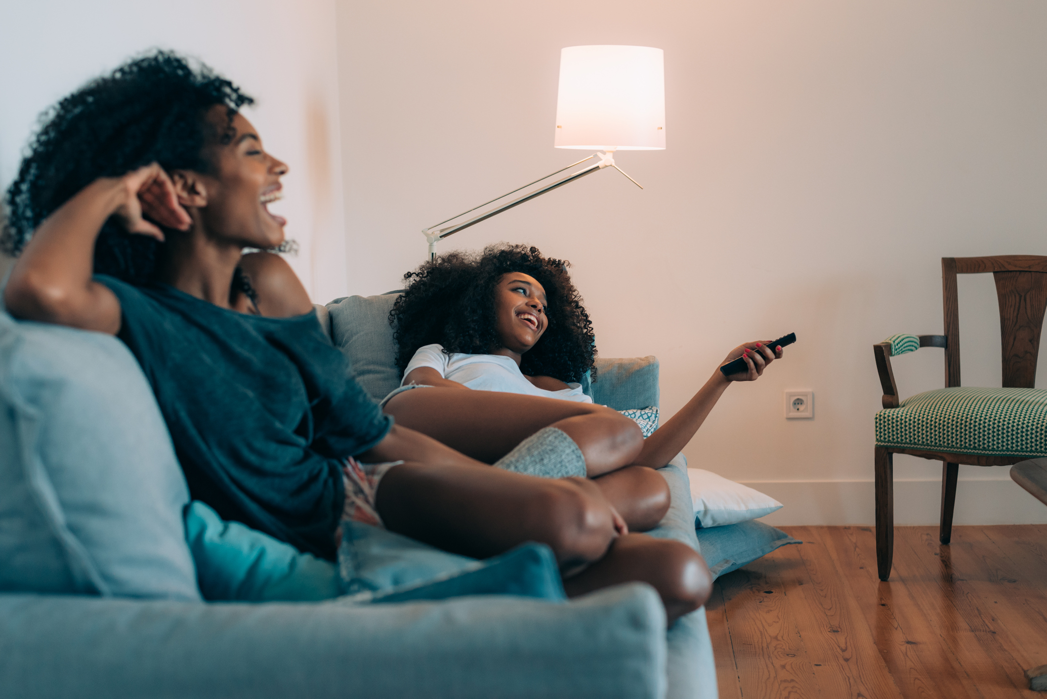 Two Black women laughing and watching tv on the couch